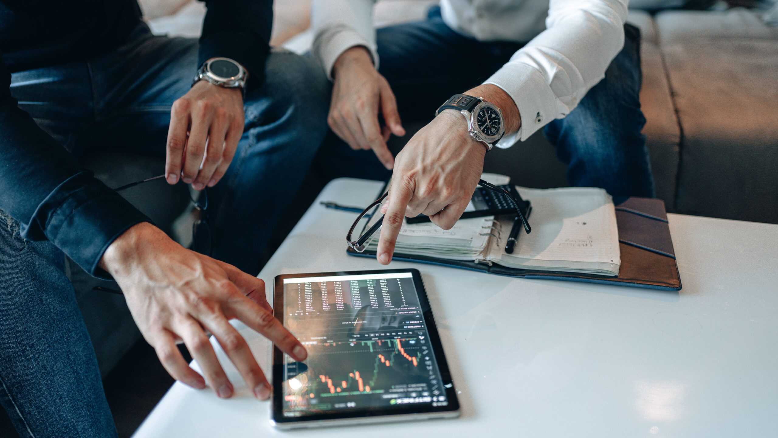 Two men reviewing stock market data on a tablet, pointing at charts.